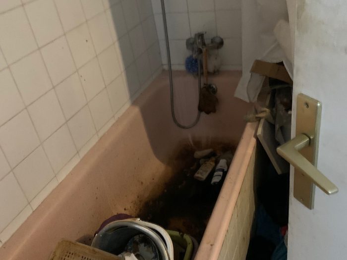 Salle de bain insalubre avec une baignoire remplie de déchets nécessitant un nettoyage.